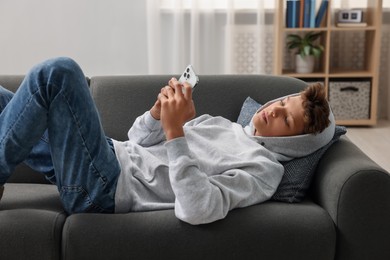 Photo of Loneliness concept. Sad teenage boy using smartphone on sofa at home