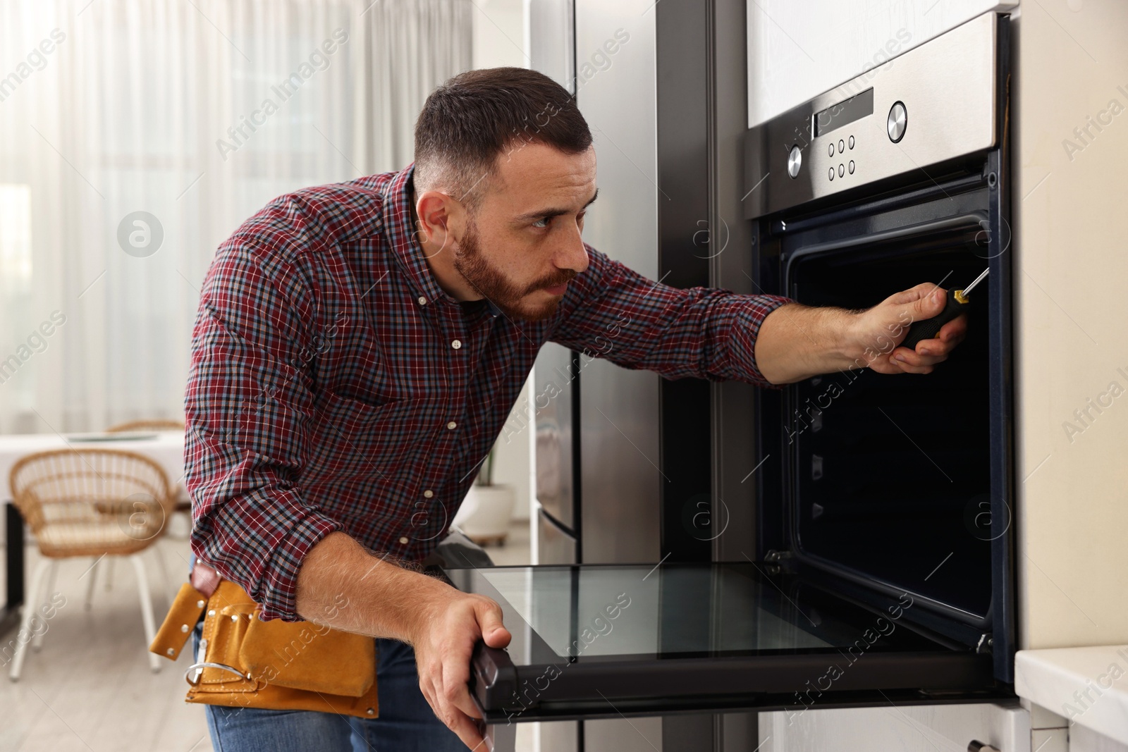 Photo of Repairman with screwdriver fixing oven at home