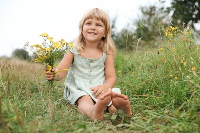 Photo of Barefoot little girl with flowers at meadow. Child enjoying beautiful nature