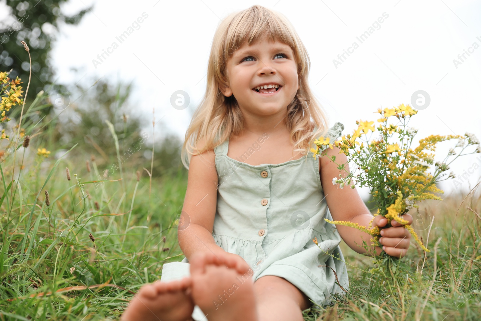 Photo of Barefoot little girl with flowers at meadow. Child enjoying beautiful nature