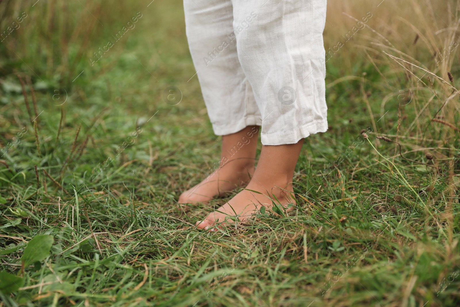 Photo of Little child standing barefoot on green grass outdoors, closeup. Enjoying nature