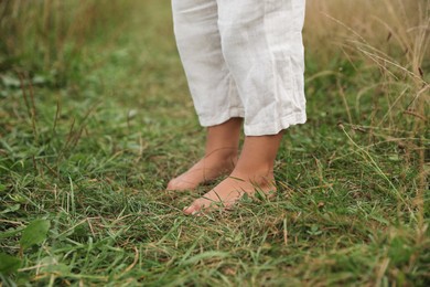 Photo of Little child standing barefoot on green grass outdoors, closeup. Enjoying nature