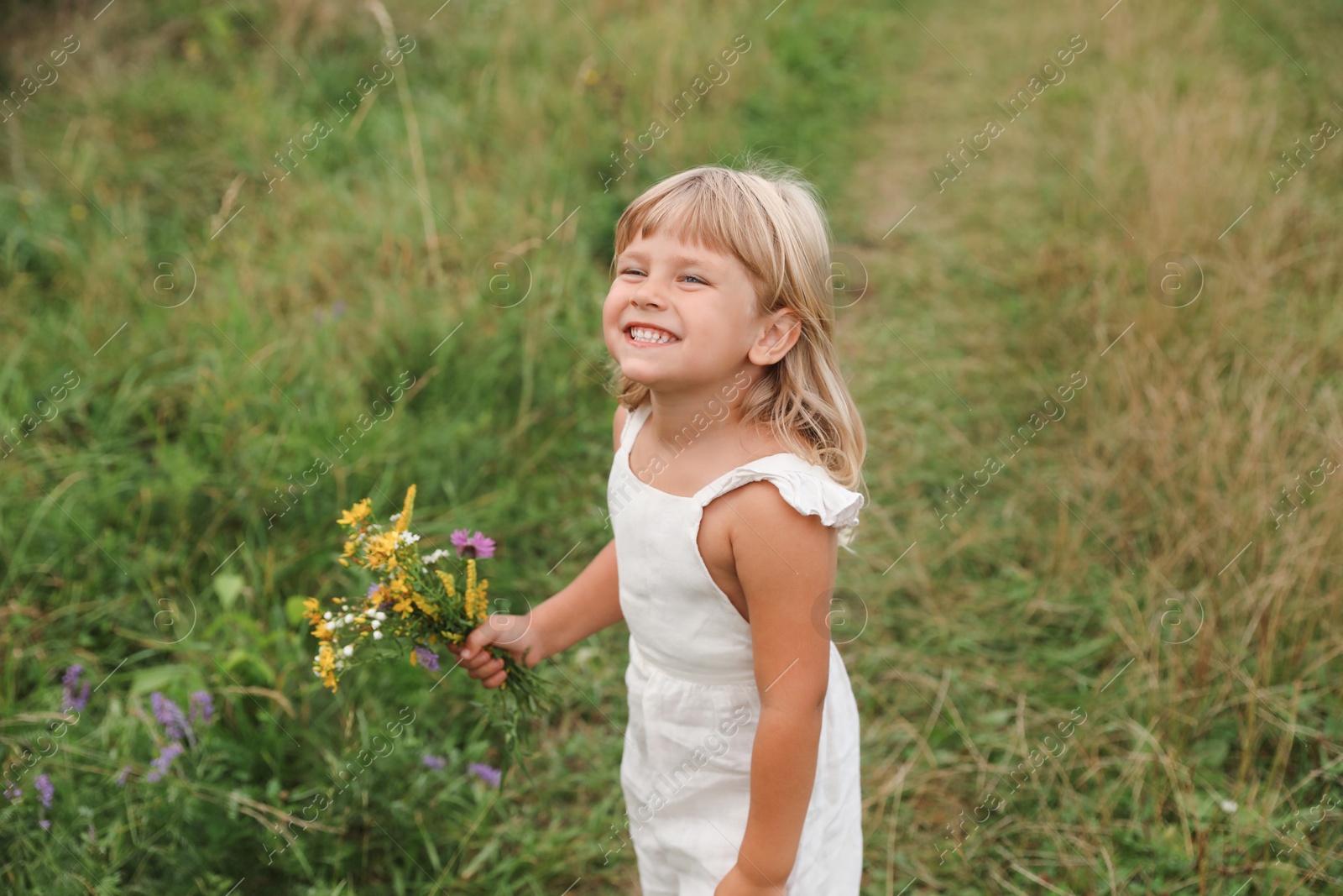 Photo of Cute little girl with flowers at meadow. Child enjoying beautiful nature