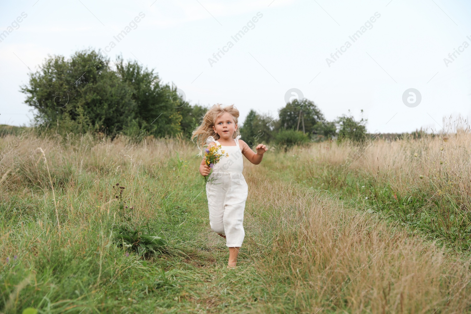 Photo of Cute little girl with flowers walking barefoot at meadow. Enjoying beautiful nature