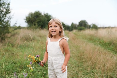 Cute little girl with flowers at meadow. Child enjoying beautiful nature