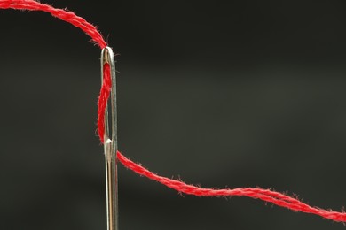 Sewing needle with red thread on black background, closeup. Space for text