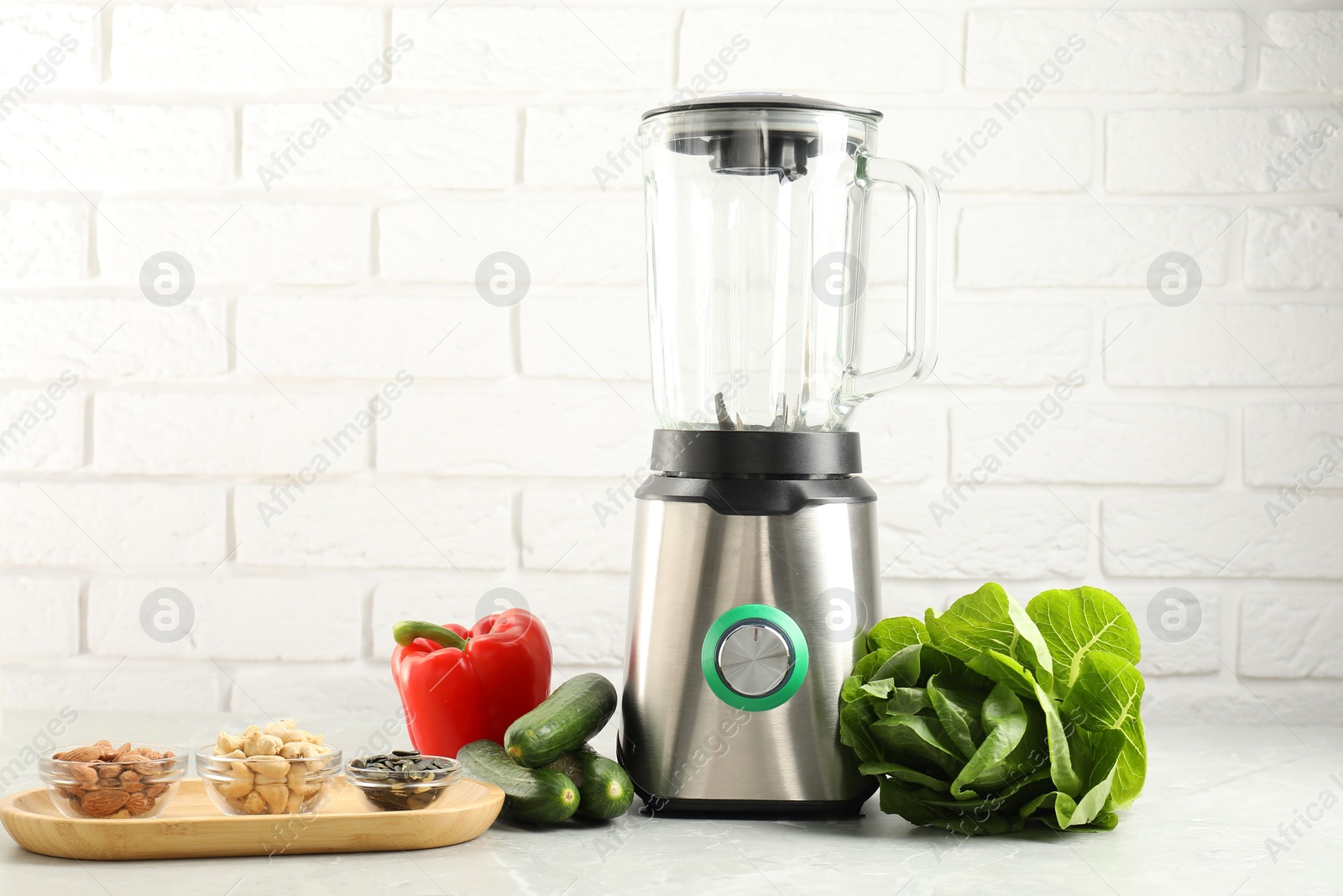 Photo of Blender and products on light table against white brick wall