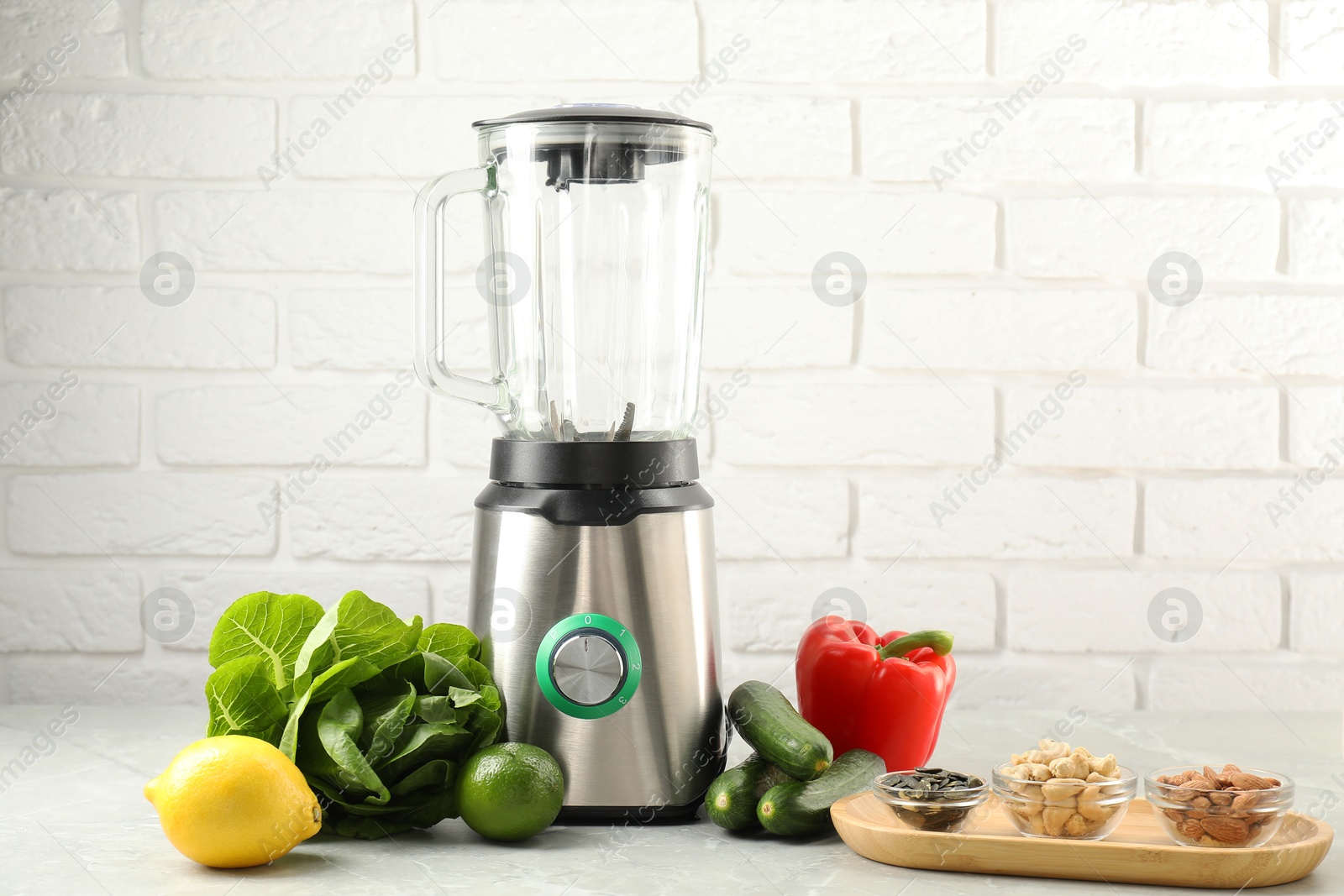 Photo of Blender and products on light table against white brick wall