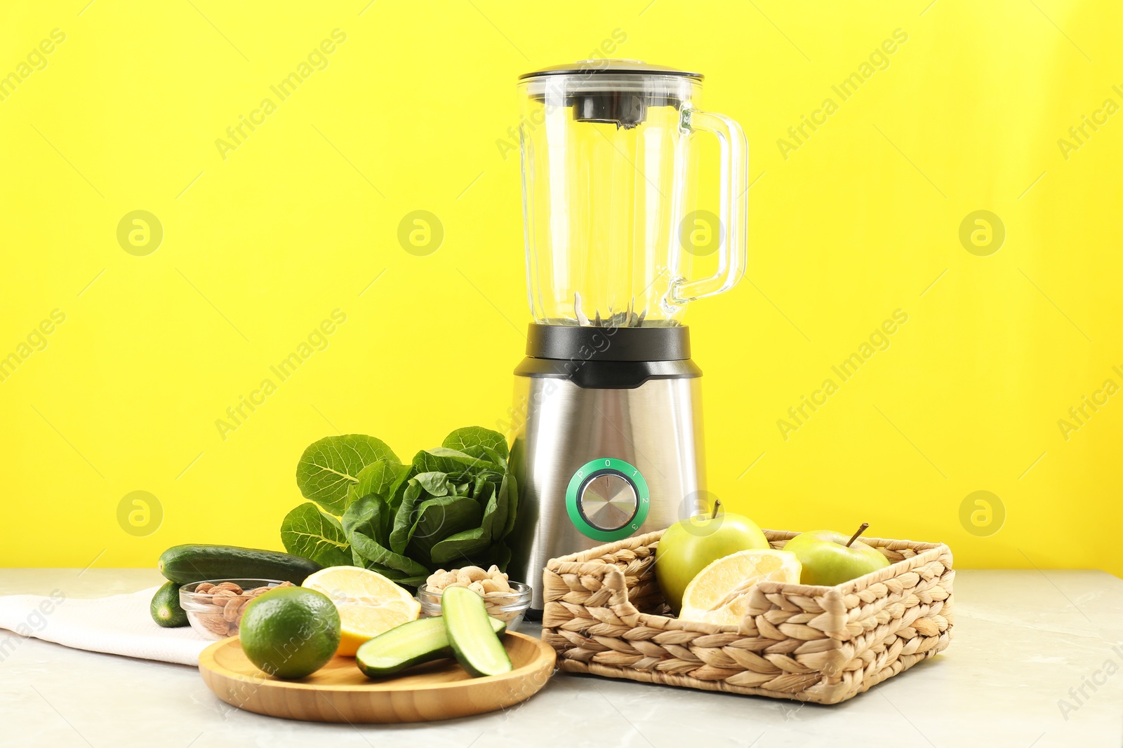 Photo of Blender and products on grey table against yellow background