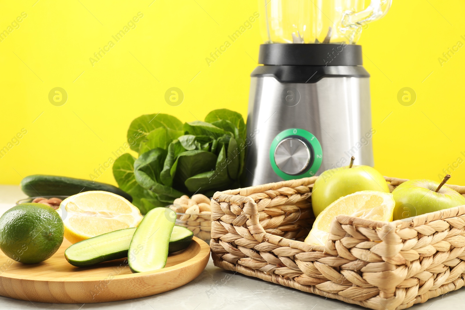 Photo of Blender and products on grey table against yellow background, closeup