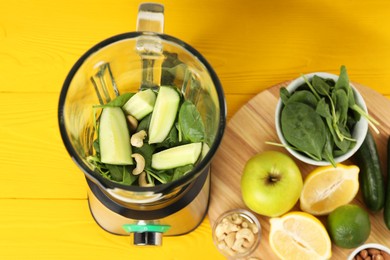 Photo of Modern blender with ingredients for smoothie on yellow wooden table, top view