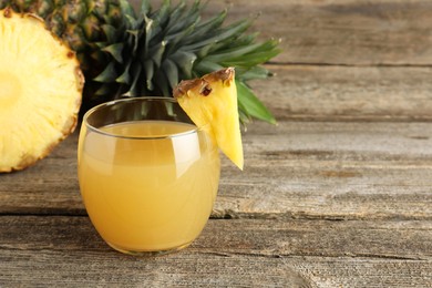 Photo of Tasty pineapple juice in glass and fresh fruit on wooden table, closeup. Space for text