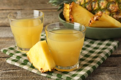 Photo of Tasty pineapple juice in glasses and slice of fresh fruit on wooden table, closeup