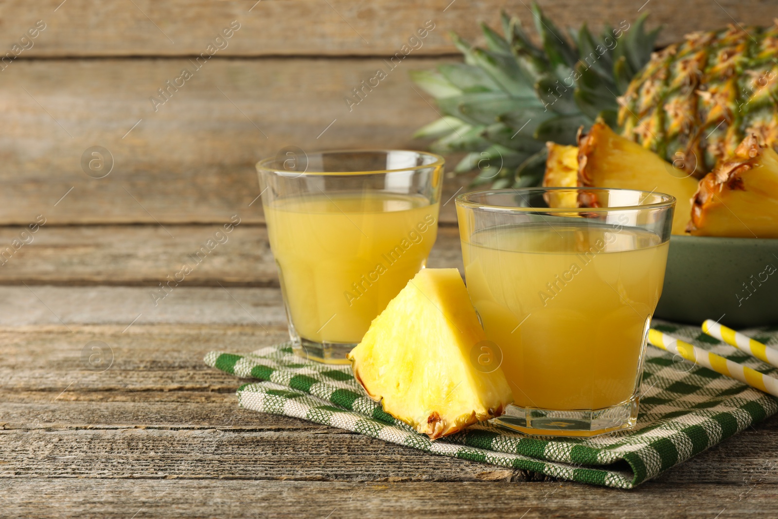 Photo of Tasty pineapple juice in glasses and slice of fresh fruit on wooden table, closeup. Space for text