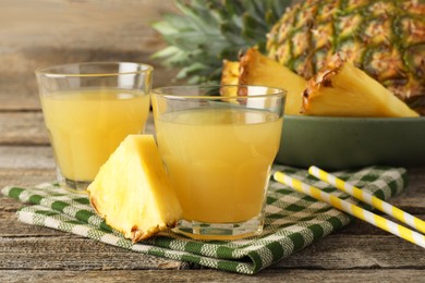 Photo of Tasty pineapple juice in glasses and slice of fresh fruit on wooden table, closeup