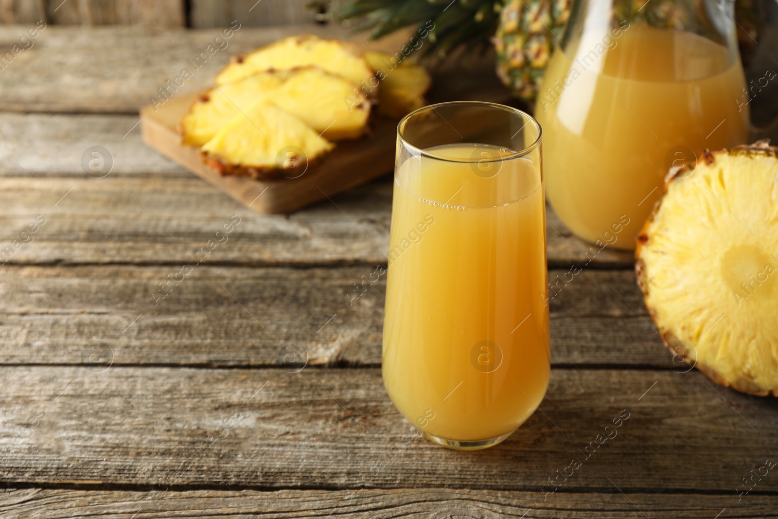 Photo of Tasty pineapple juice in glass and fresh fruit on wooden table, closeup. Space for text