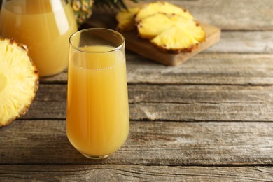 Photo of Tasty pineapple juice in glass and fresh fruit on wooden table, closeup. Space for text