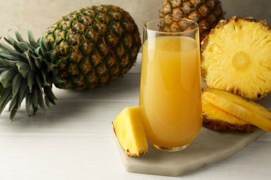 Photo of Tasty pineapple juice in glass and fresh fruits on white wooden table against grey background, closeup