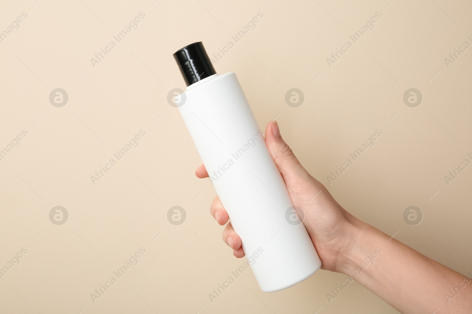 Photo of Woman with shampoo bottle on beige background, closeup