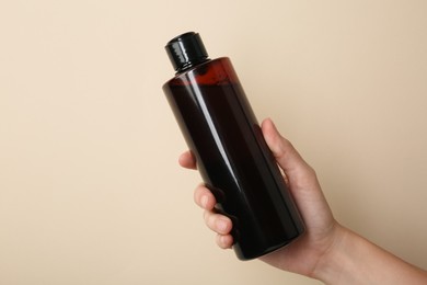 Photo of Woman with shampoo bottle on beige background, closeup