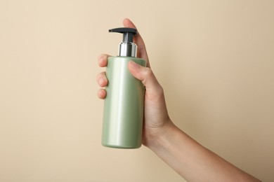 Photo of Woman with shampoo bottle on beige background, closeup