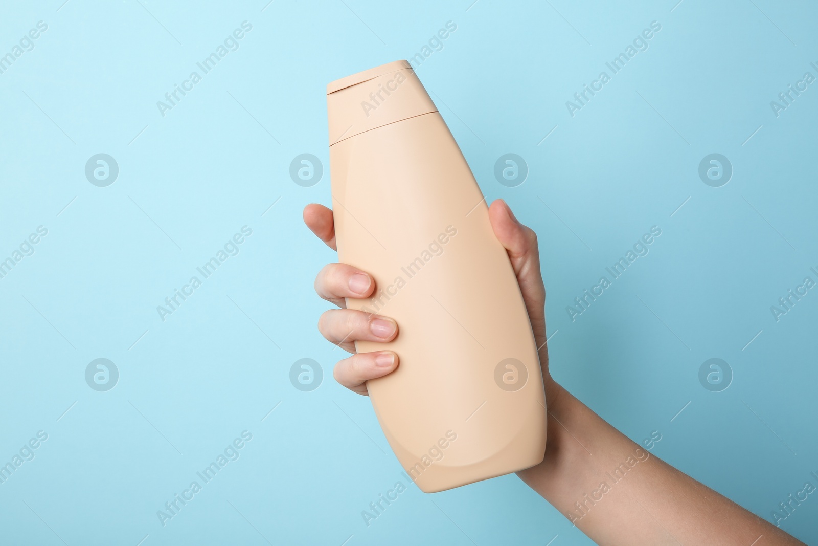 Photo of Woman with shampoo bottle on light blue background, closeup