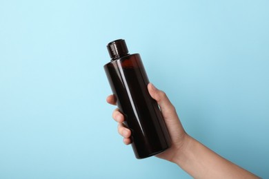 Photo of Woman with shampoo bottle on light blue background, closeup