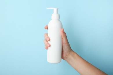 Photo of Woman with shampoo bottle on light blue background, closeup