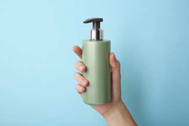 Photo of Woman with shampoo bottle on light blue background, closeup