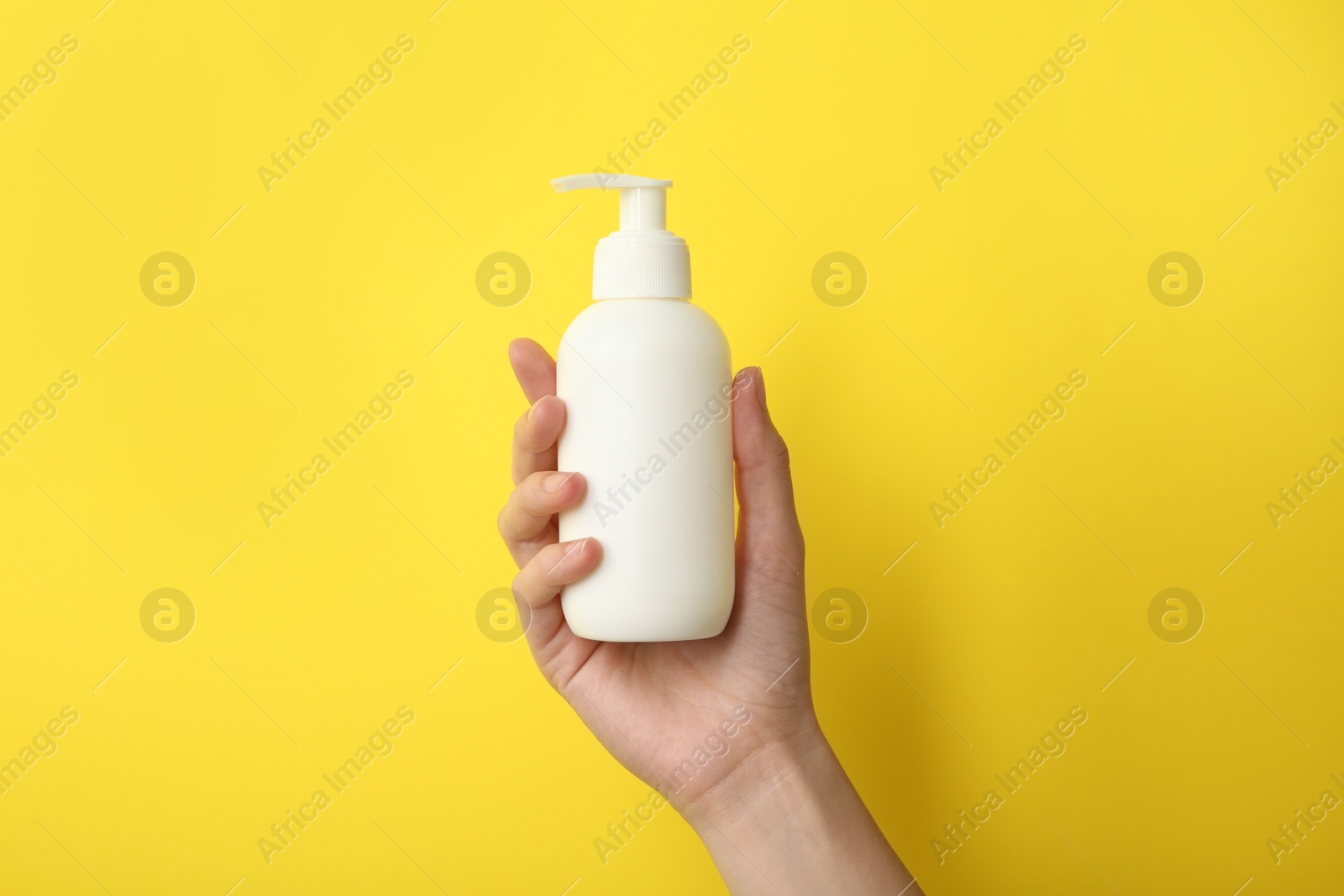 Photo of Woman with shampoo bottle on yellow background, closeup