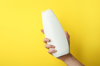 Photo of Woman with shampoo bottle on yellow background, closeup