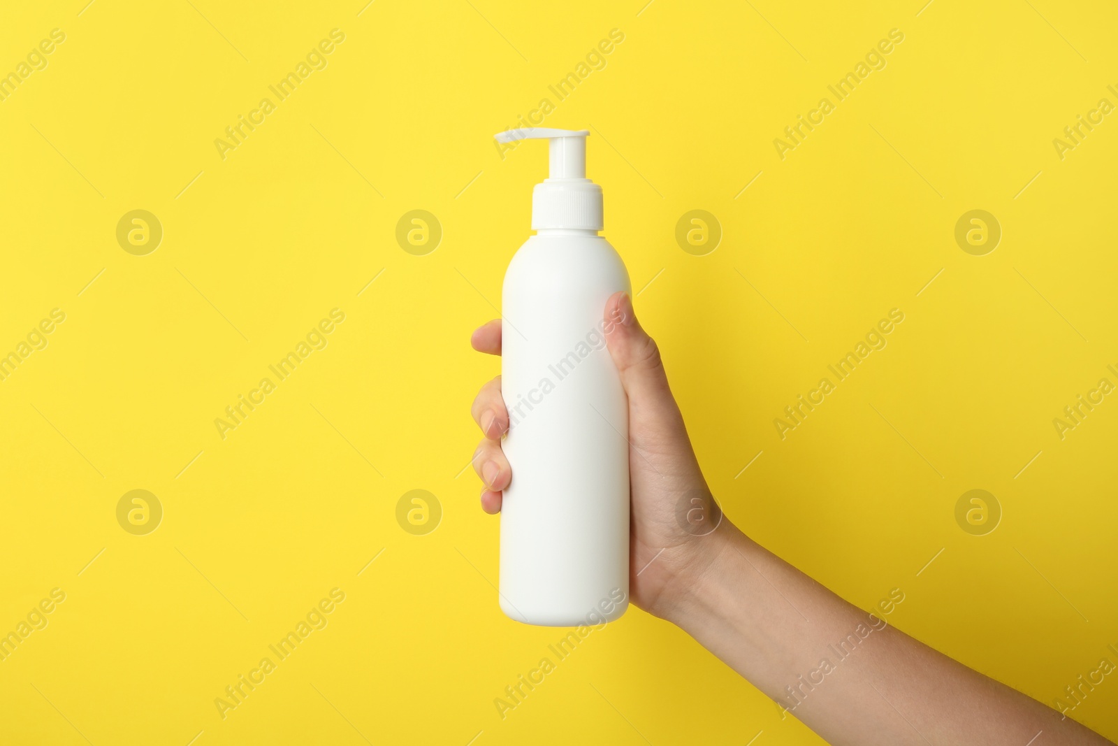 Photo of Woman with shampoo bottle on yellow background, closeup