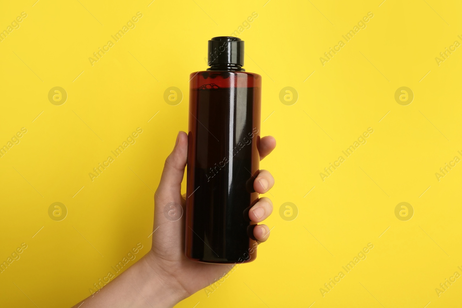 Photo of Woman with shampoo bottle on yellow background, closeup