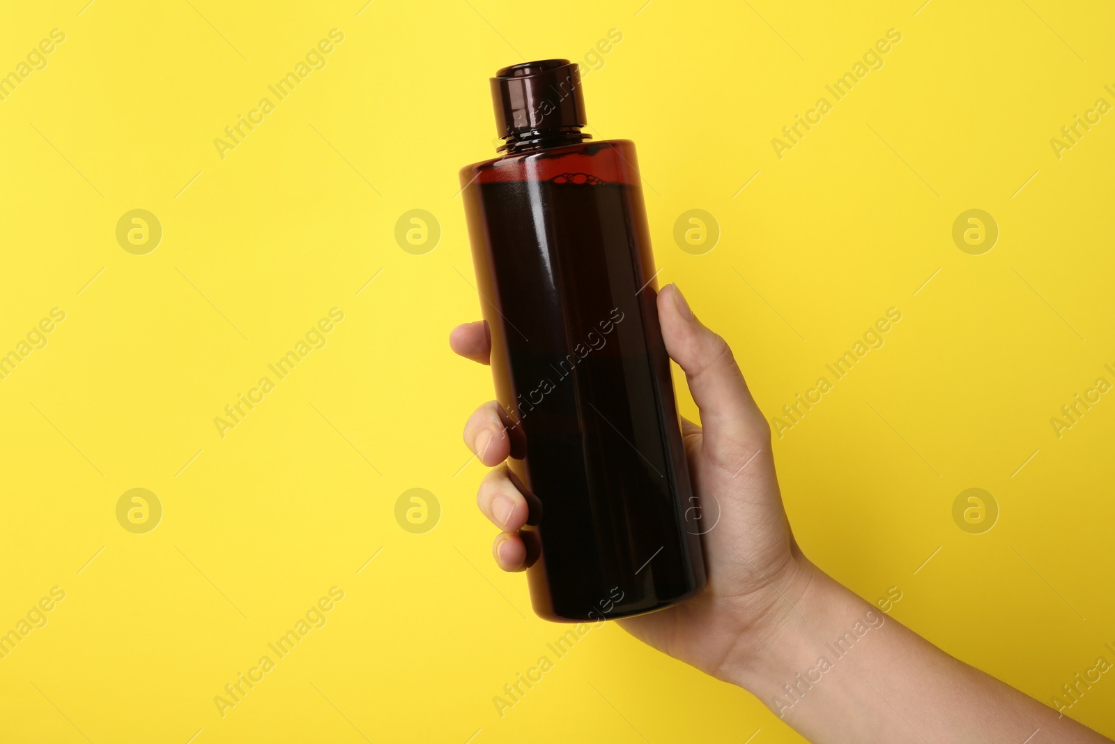 Photo of Woman with shampoo bottle on yellow background, closeup