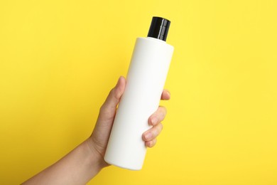 Photo of Woman with shampoo bottle on yellow background, closeup