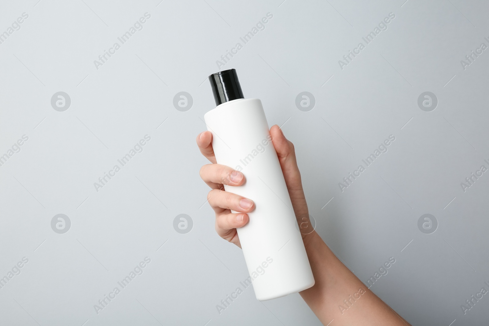 Photo of Woman with shampoo bottle on grey background, closeup