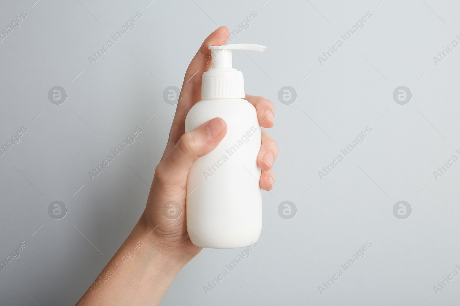 Photo of Woman with shampoo bottle on grey background, closeup