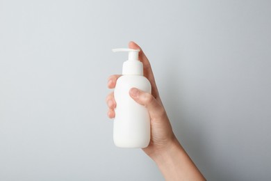 Photo of Woman with shampoo bottle on grey background, closeup