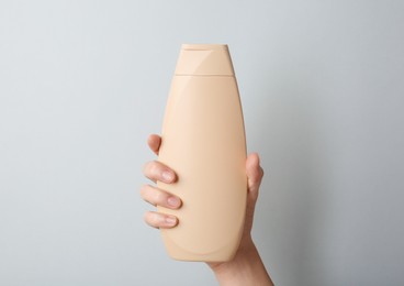 Photo of Woman with shampoo bottle on grey background, closeup