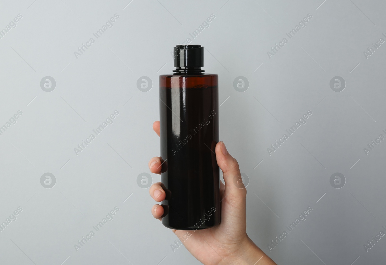 Photo of Woman with shampoo bottle on grey background, closeup