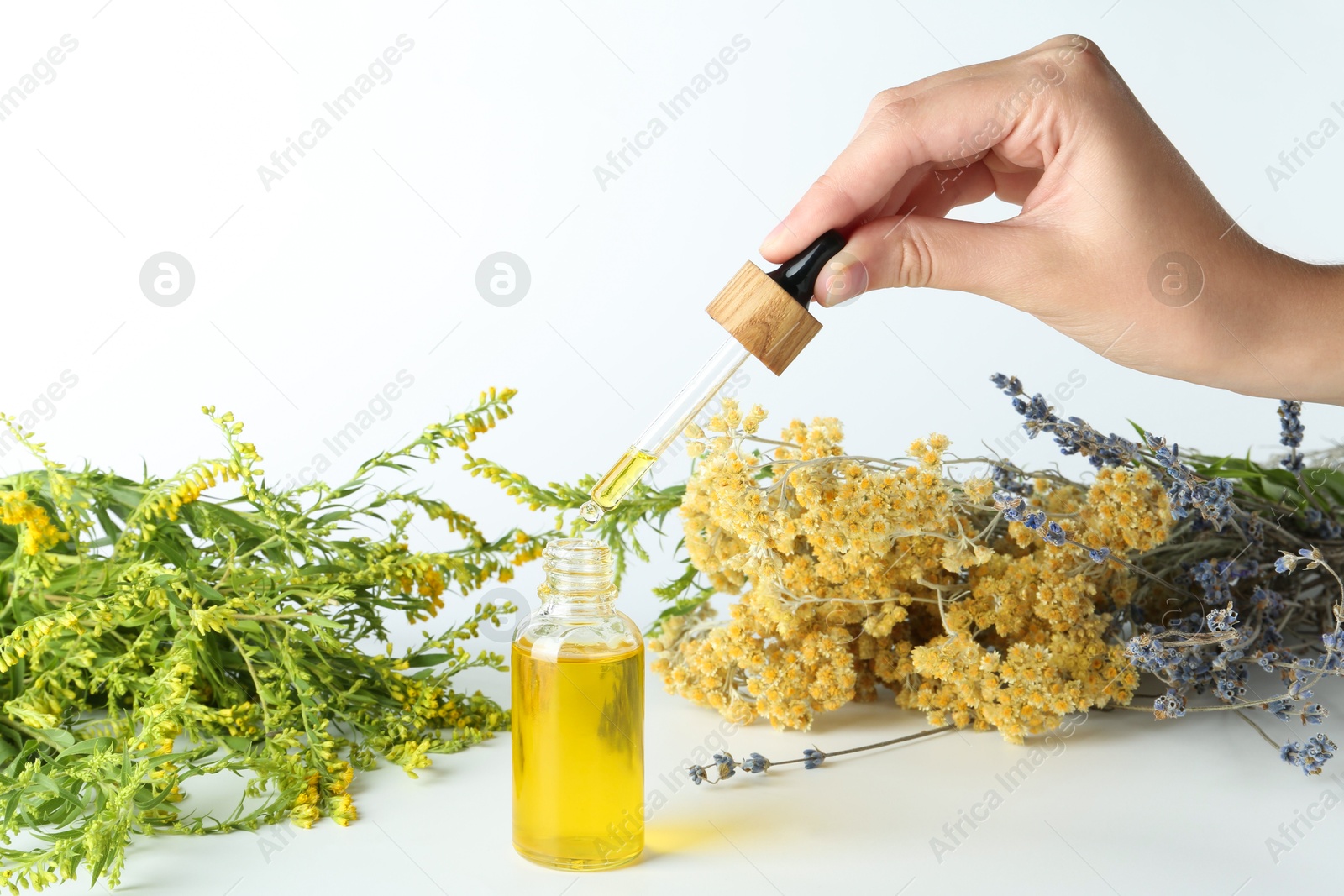 Photo of Woman dripping tincture from pipette into bottle and herbs on white background, closeup