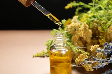 Photo of Dripping tincture from pipette into bottle and herbs against color background, closeup