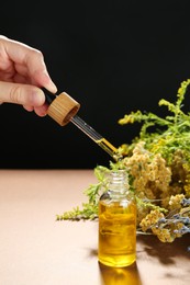 Photo of Woman dripping tincture from pipette into bottle and herbs against color background, closeup