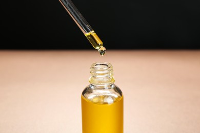 Photo of Dripping tincture from pipette into bottle against color background, closeup