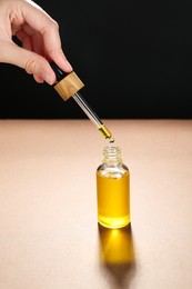 Photo of Woman dripping tincture from pipette into bottle on color background, closeup