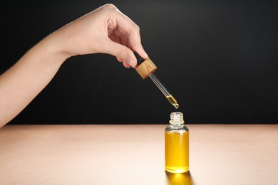 Photo of Woman dripping tincture from pipette into bottle on color background, closeup