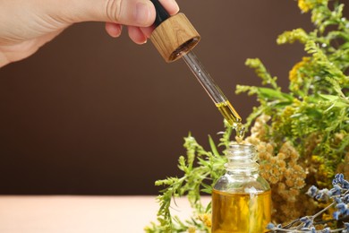 Photo of Woman dripping tincture from pipette into bottle and herbs against color background, closeup