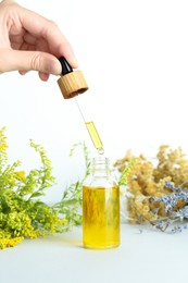 Photo of Woman dripping tincture from pipette into bottle and herbs on white background, closeup