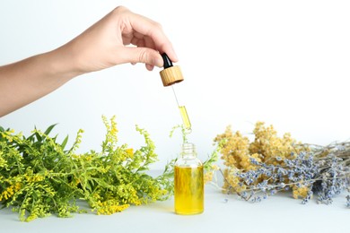 Photo of Woman dripping tincture from pipette into bottle and herbs on white background, closeup