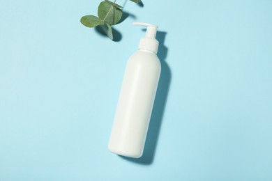 Photo of Bottle of shampoo and eucalyptus leaves on light blue background, flat lay